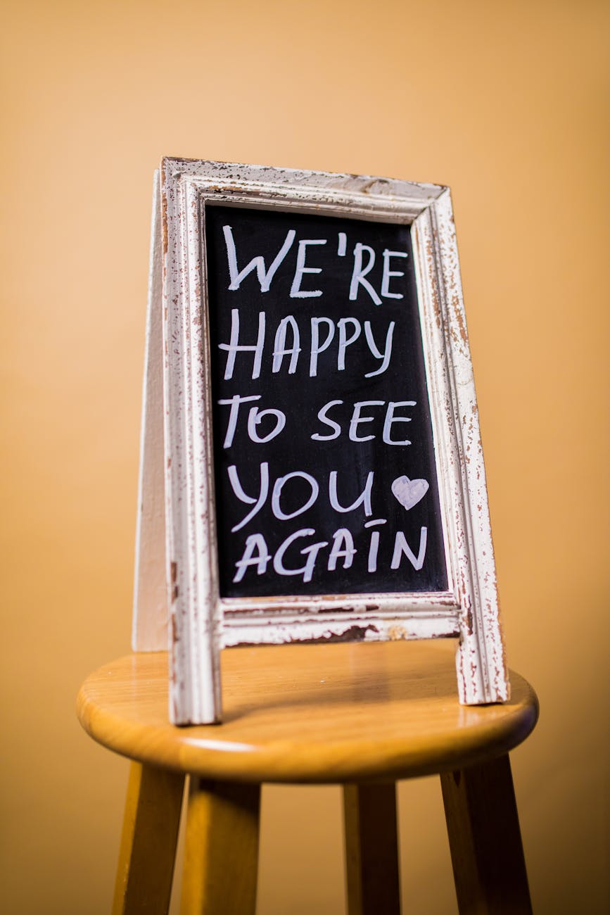 Weathered chalkboard with 'We're happy to see you again' message, resting on a wooden stool.