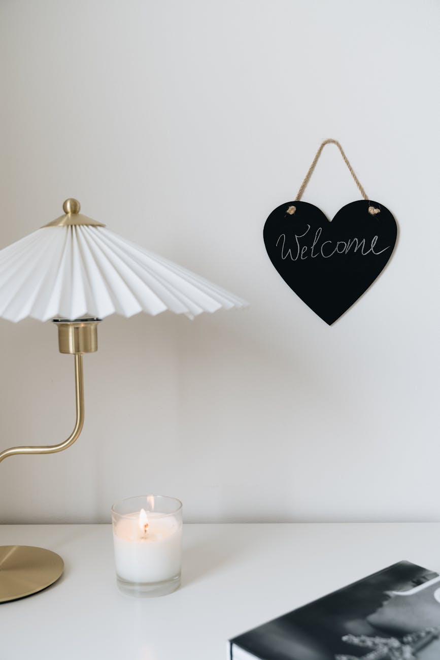 A cozy minimalist setting with a lamp, candle, and welcome sign on a wall.